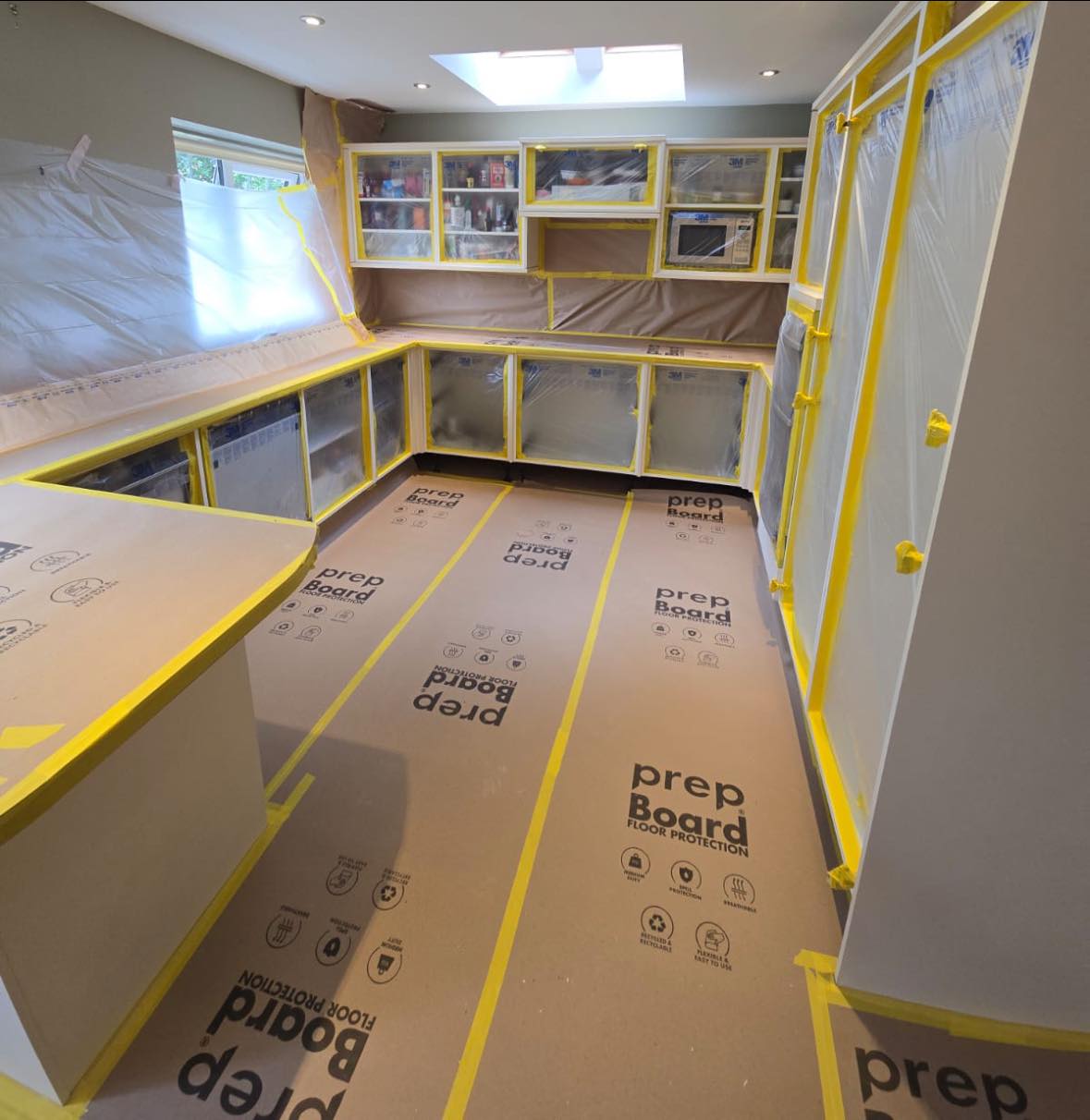 Kitchen fully masked up with yellow tape, plastic sheeting and floor protection — ready for in-situ spray on Day 4